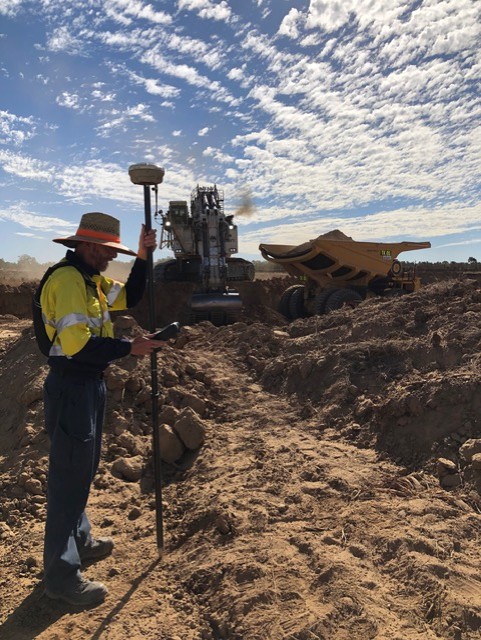 GPS rover survey beside excavator and haul truck on a mine site
